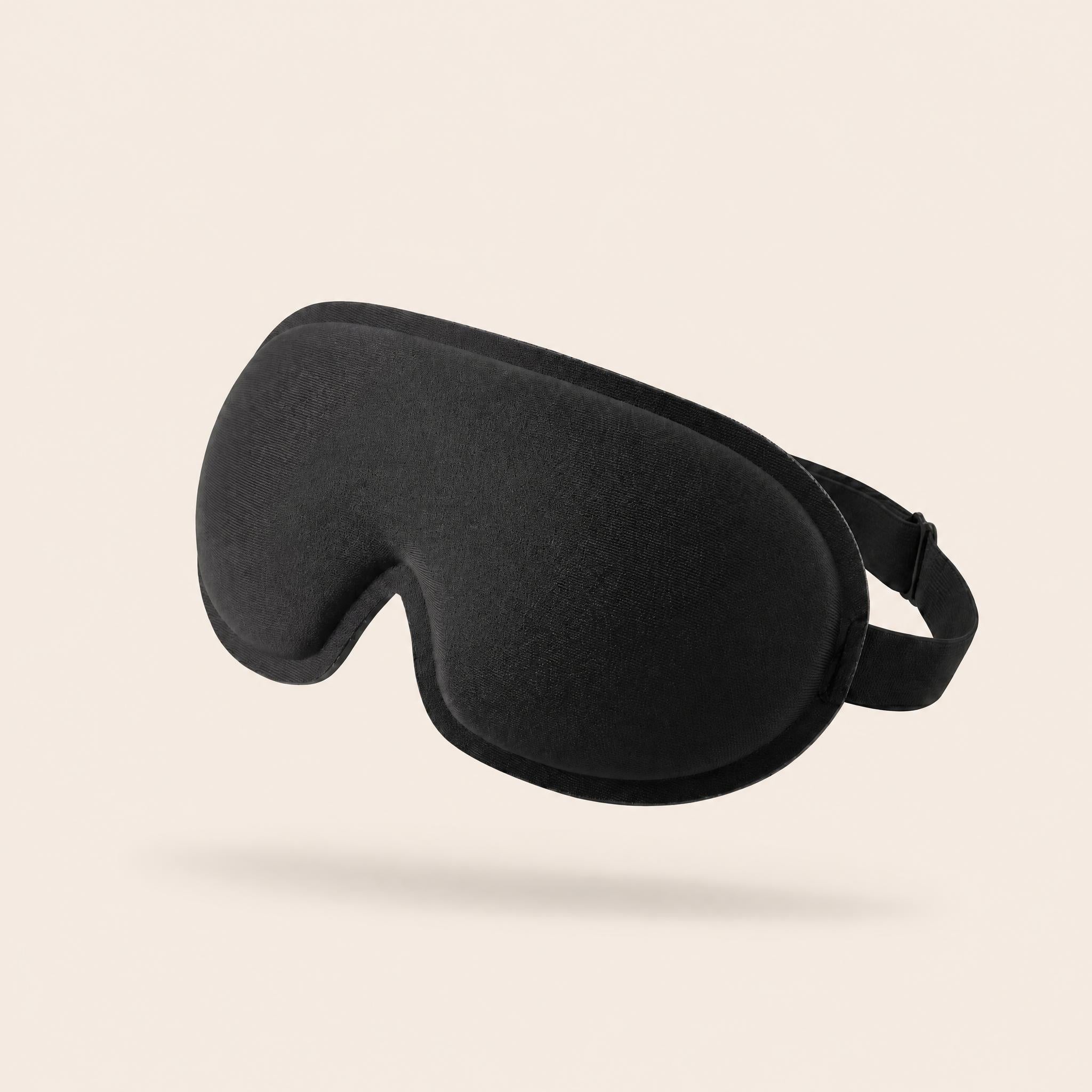 Black Somnia Sable Mask with a curved padded front and elastic strap on a warm cream background.